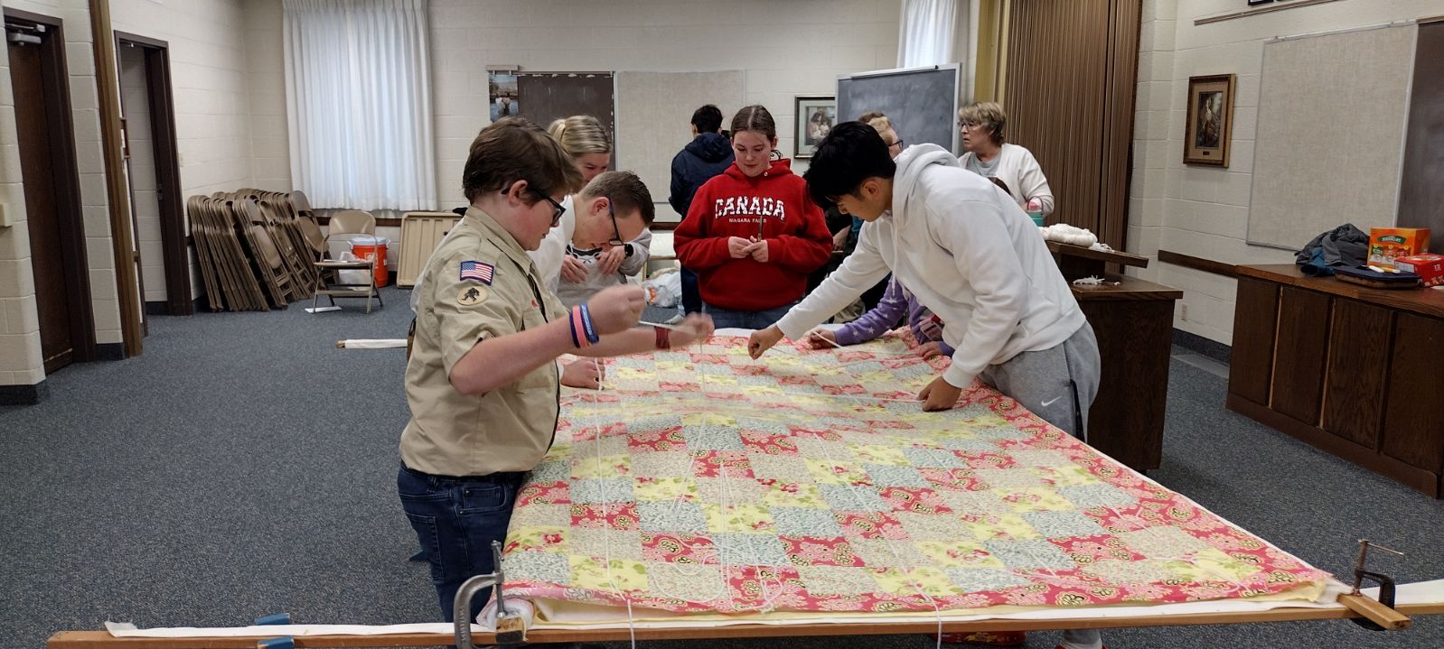 Volunteers tying a handmade quilt inside a church room
