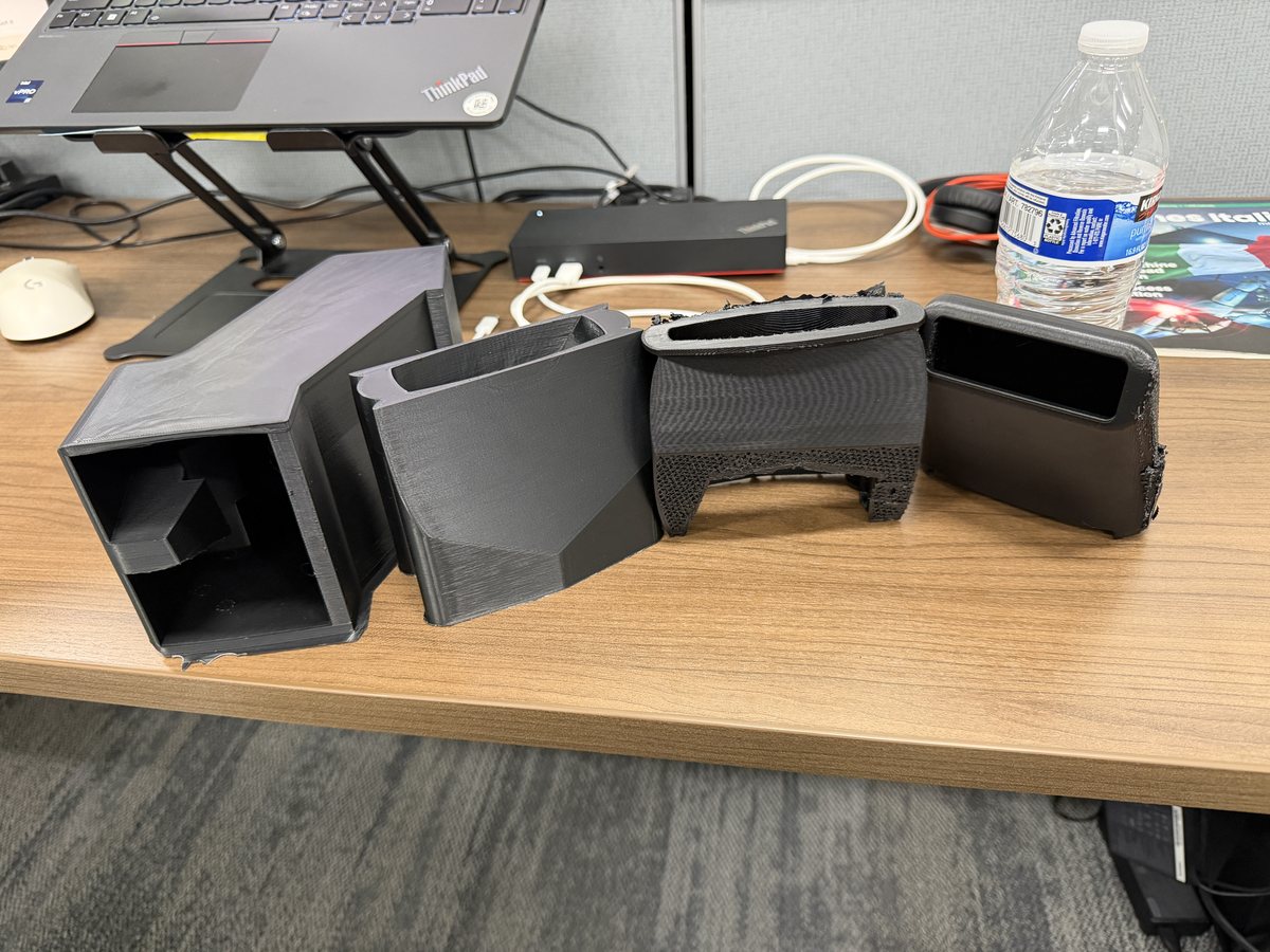 Several black 3D printed Quick Quack nozzle prototype parts on a desk